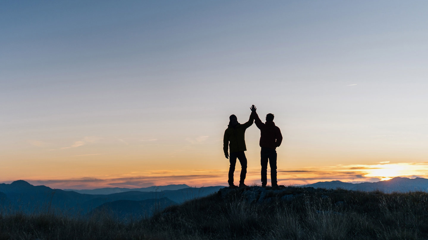 To personer giver high five på toppen af et bjerg